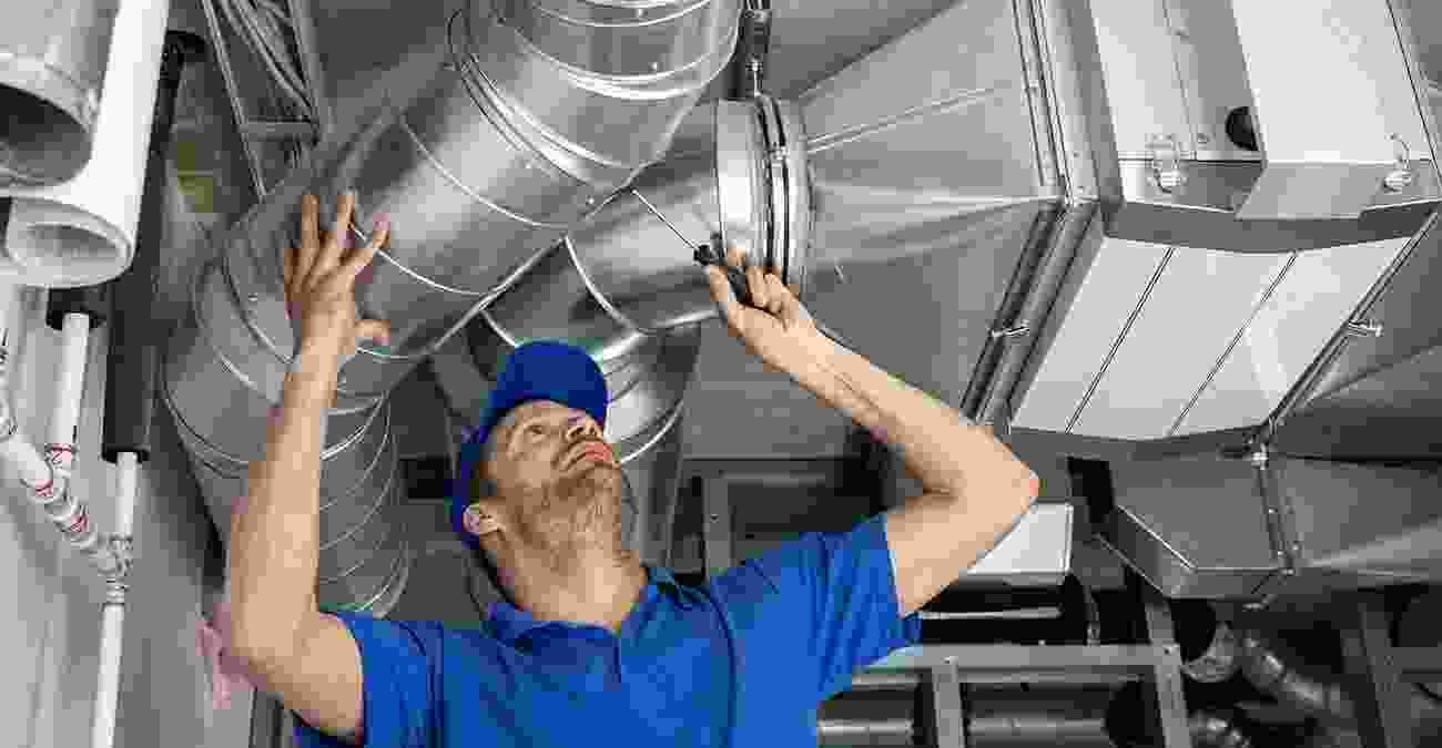 HVAC technician inspecting air conditioning ductwork and performing maintenance in a residential setting.